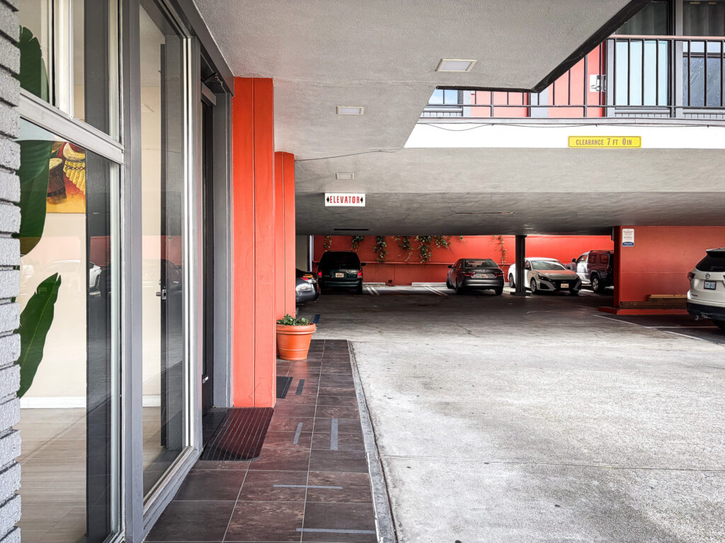 Covered parking area and lobby entrance at La Luna Inn in San Francisco, with an elevator sign visible and orange accent columns throughout the property.